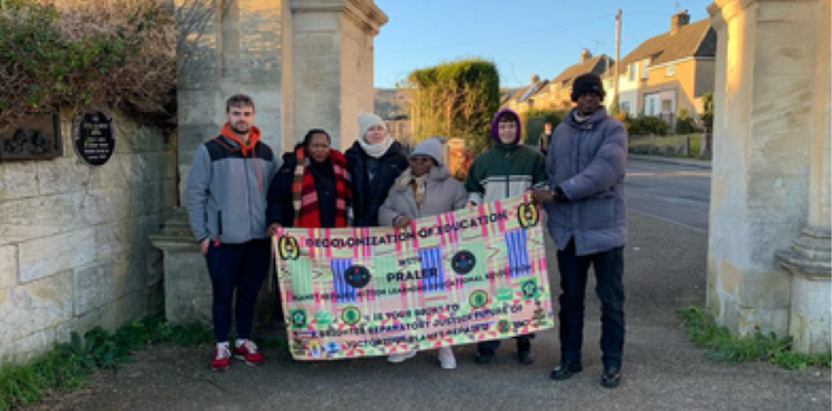 Six people standing at the Anti-slavery arch, holding up a banner that reads: PRALER - decolonization of eduction